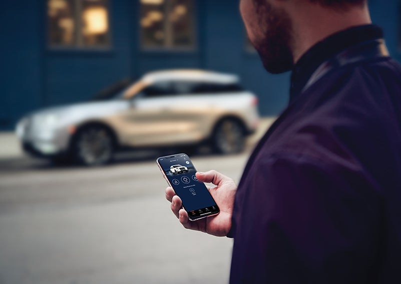 A person is shown interacting with a smartphone to connect to a Lincoln vehicle across the street. | Golden Circle Lincoln in Jackson TN